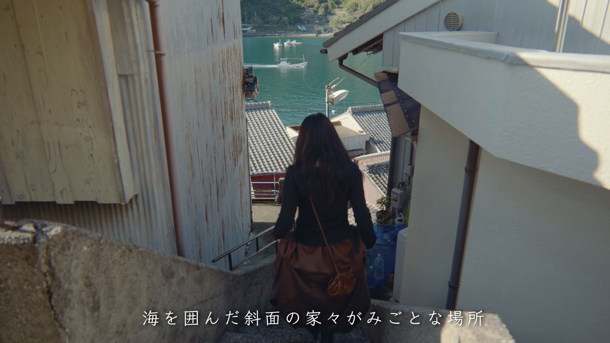 家々の間の階段を下りる後ろ姿と、下に見える湾