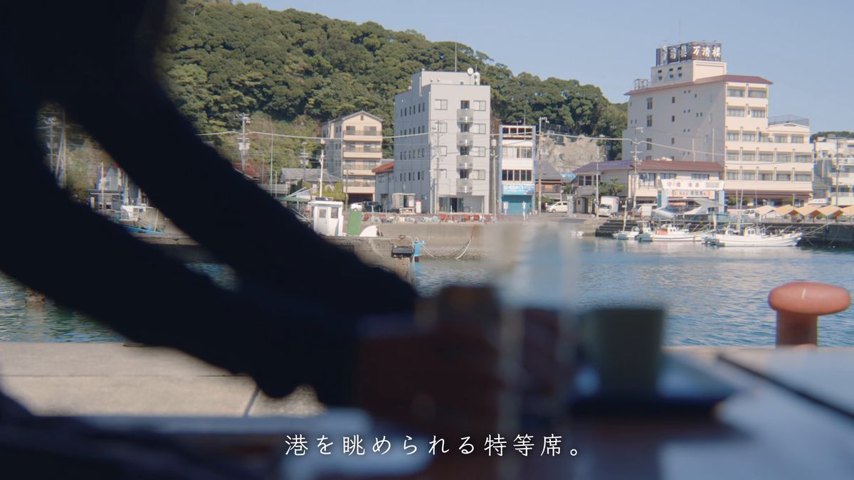 港に面した席に缶ビールを置く手元と、対岸の建物