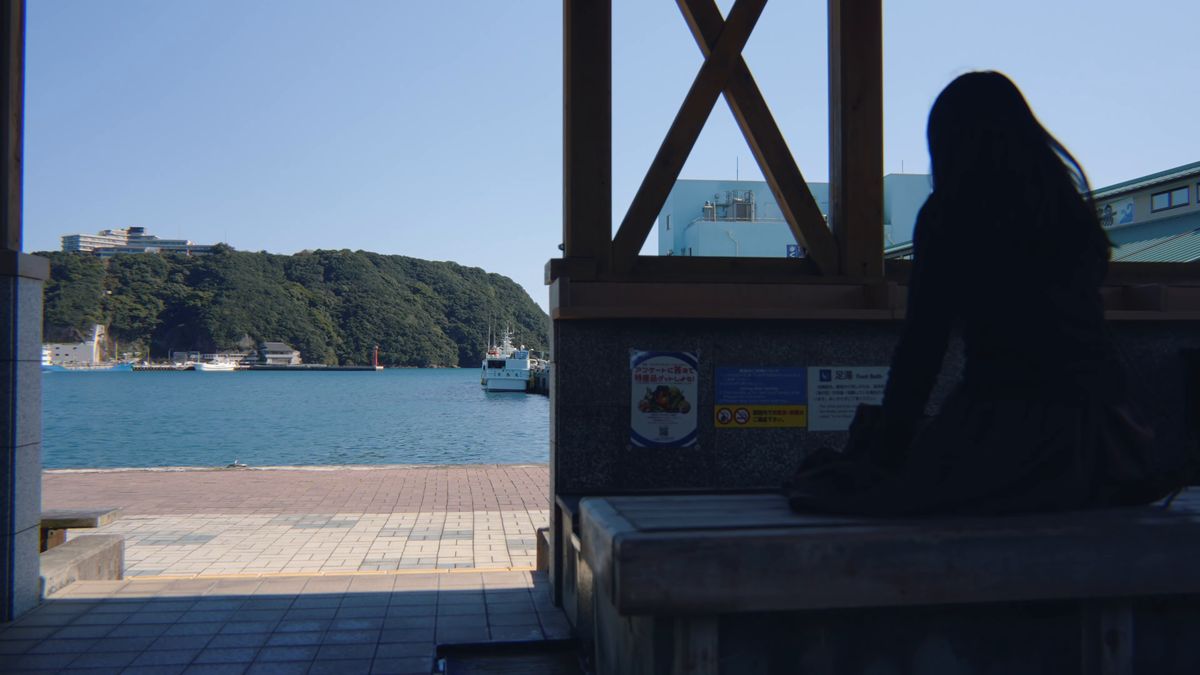 木のベンチに座って港を眺める後ろ姿