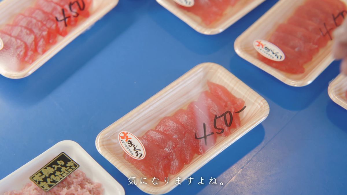 青い台に並ぶ生まぐろのパックと手書きの値段