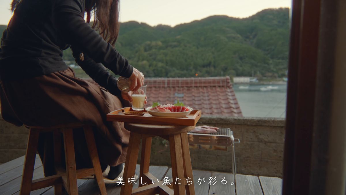 テラスの小さな机を前に座る後ろ姿と夕方の湾