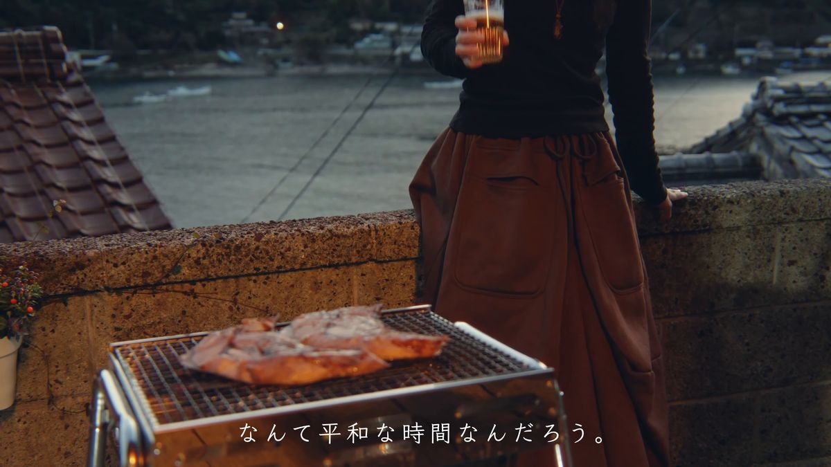七輪のそばでグラスを持つ後ろ姿と、暮れる湾