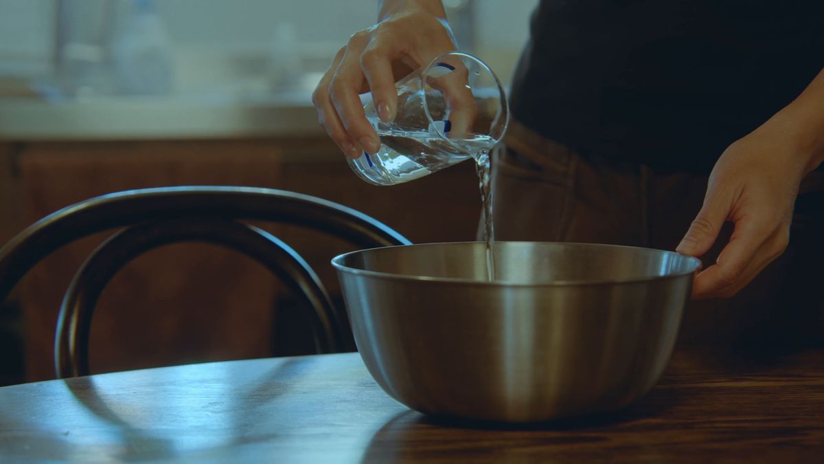 テーブルのボウルに計量カップから水を注ぐ