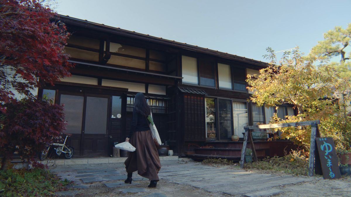 紅葉の木のそば、古民家の前に立つ後ろ姿