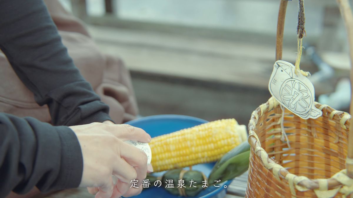 竹かごの横で温泉たまごを手にする