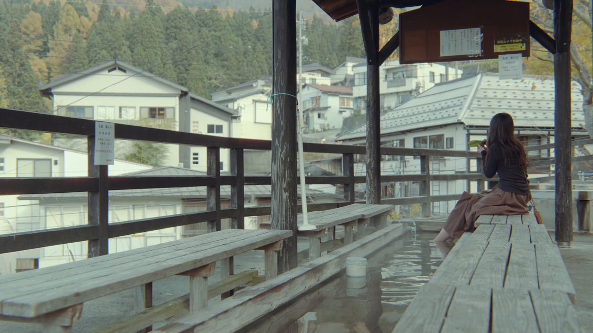 東屋のベンチに座って温泉街を眺める後ろ姿
