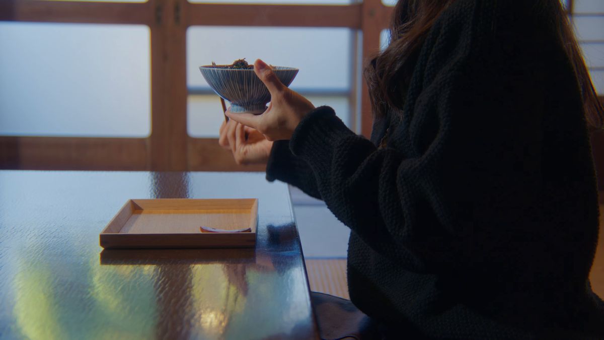 窓辺で茶碗を手に食べる後ろ姿