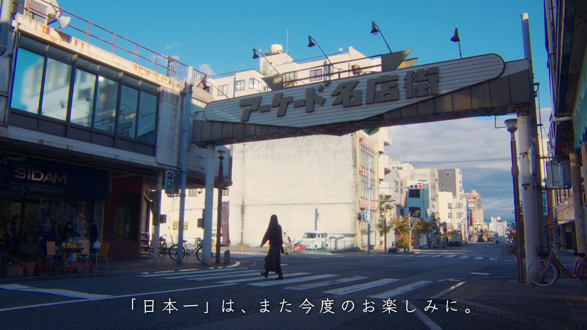 「アーケード名店街」のゲートの下の横断歩道を渡る後ろ姿