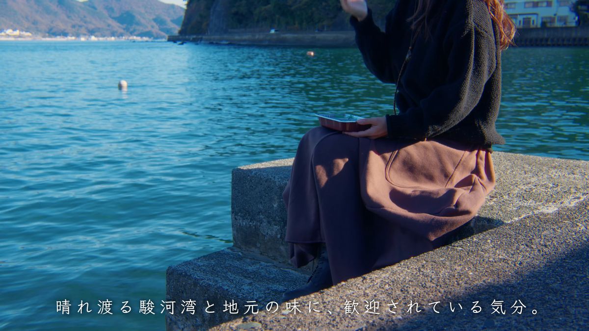 防波堤に腰かけてパックを膝にのせる後ろ姿と青い海