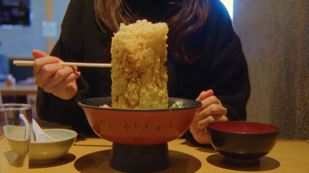 テーブルの定食と、丼の上のかき揚げを箸でつかむ