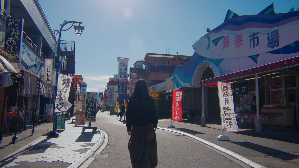 幟と看板が並ぶ魚市場前の通りを歩く後ろ姿