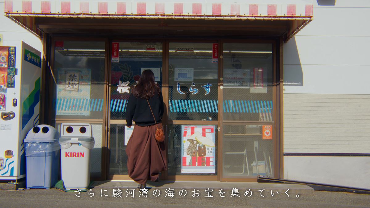 「しらす」の文字のある直売所の入口に立つ後ろ姿
