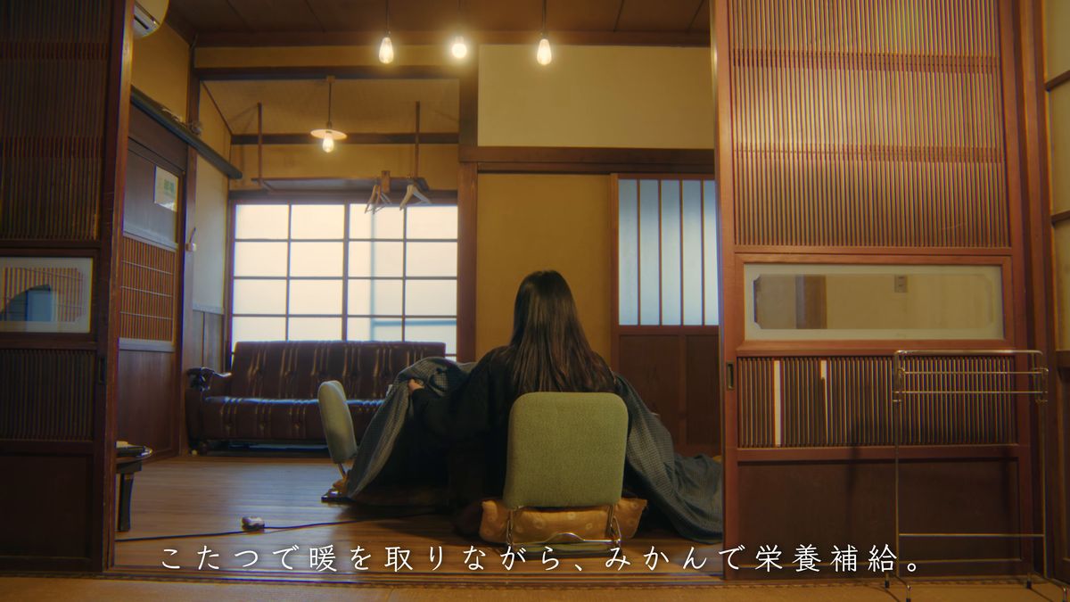 電球の下、こたつに入る後ろ姿と窓の外の海