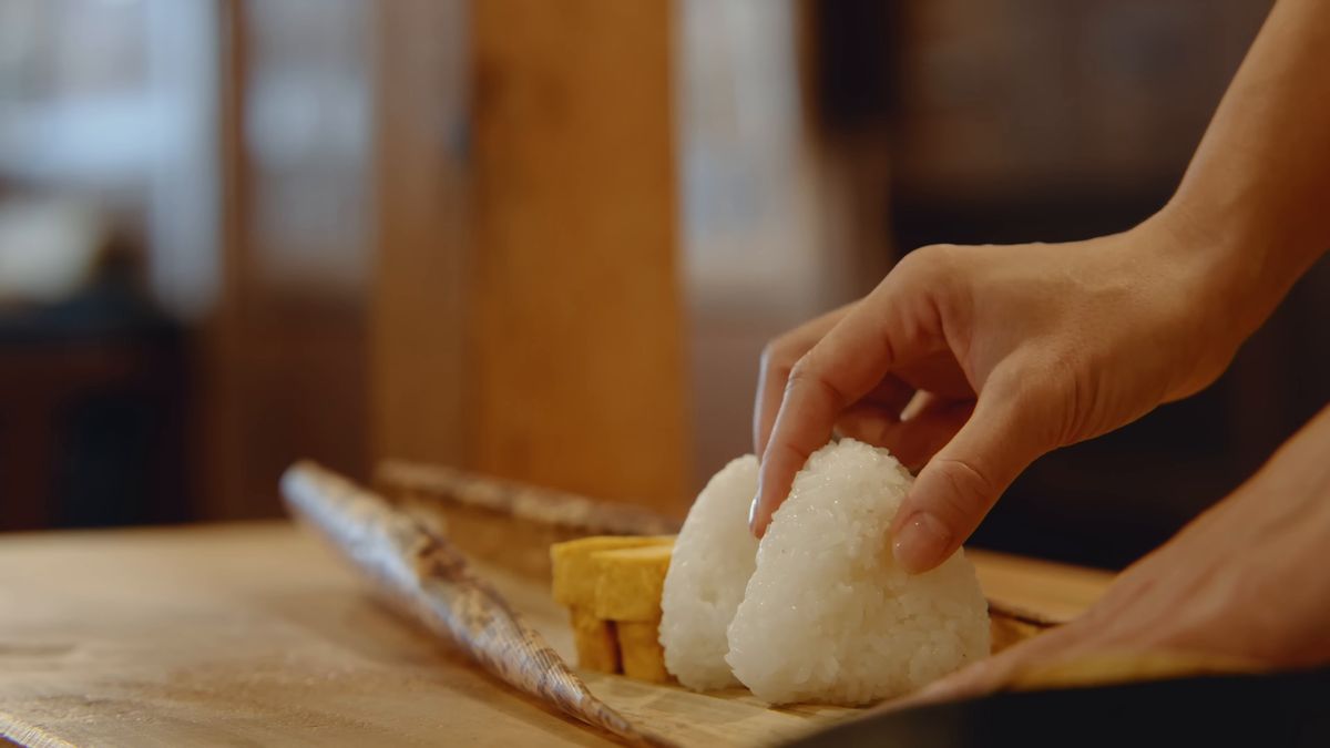 竹皮の上の卵焼きの横におにぎりを置く手元