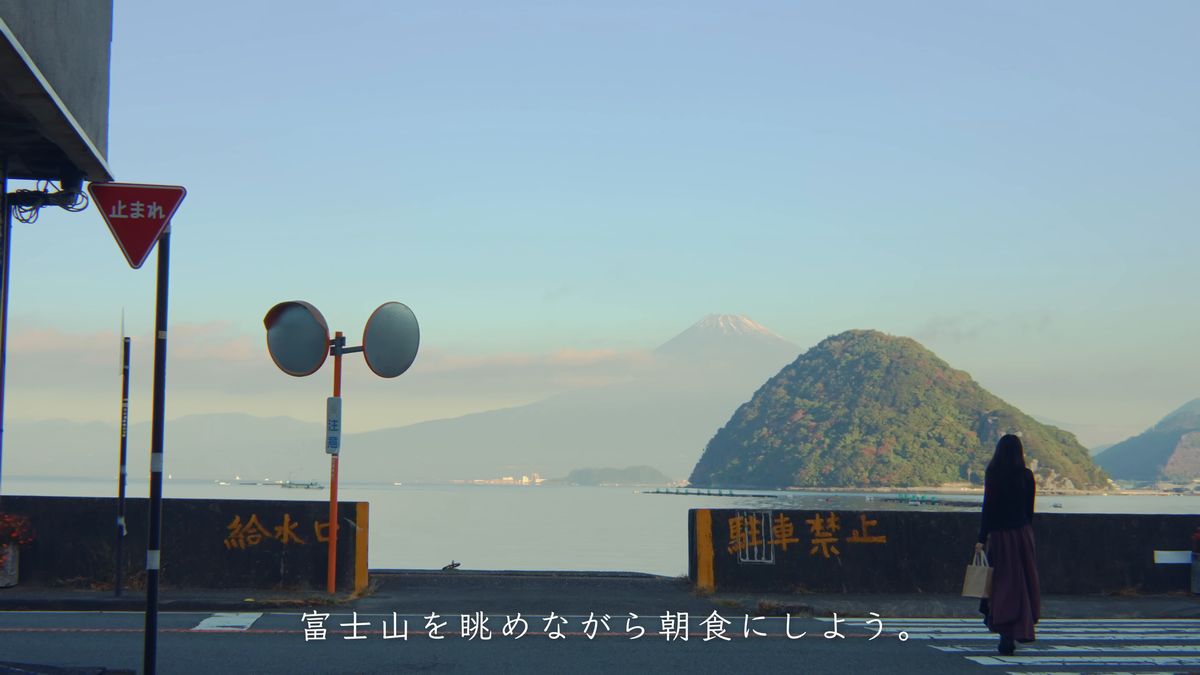 「止まれ」の標識の先に富士山と淡島、港沿いの道を歩く後ろ姿