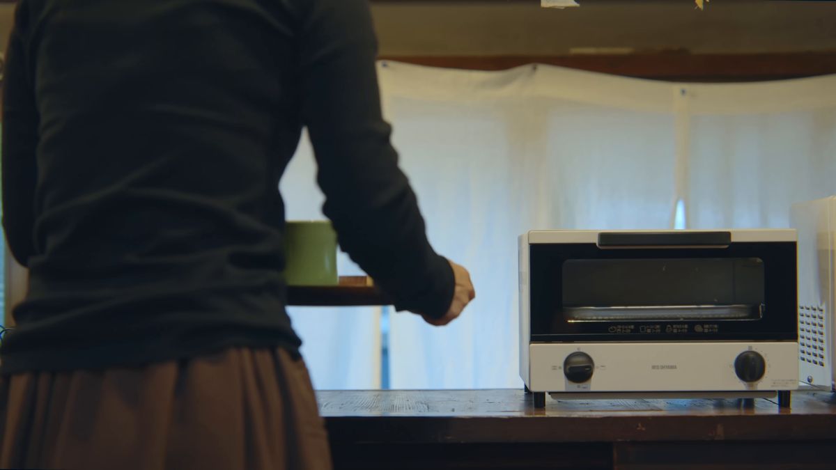 緑のカップを手にトースターの前に立つ