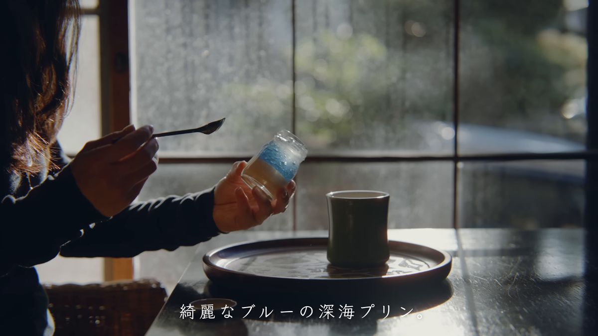 窓辺でスプーンとプリンの瓶を手にする