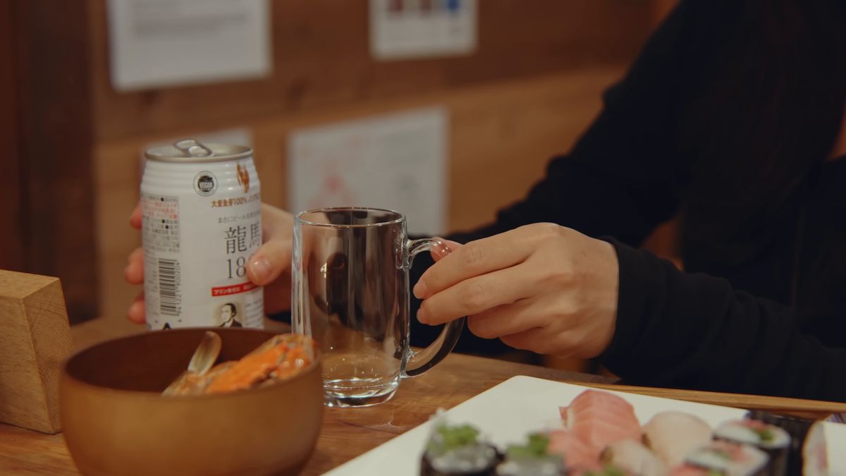 缶を片手にグラスを持ち、手前にはカニの椀