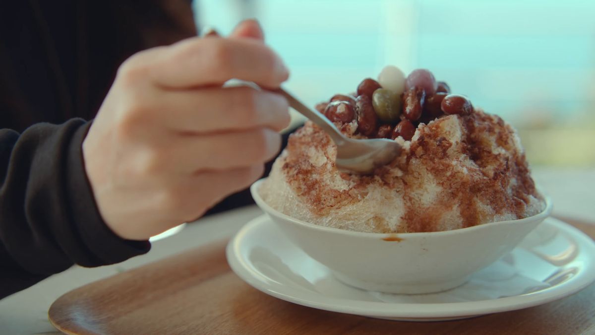 A spoon going into shaved ice topped with kintoki beans and brown sugar