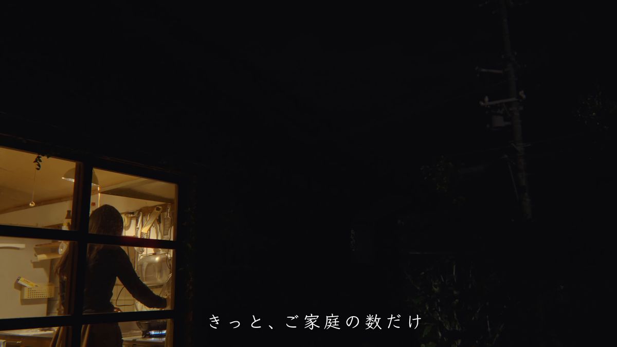 A lit window and a figure in the kitchen, seen from the dark