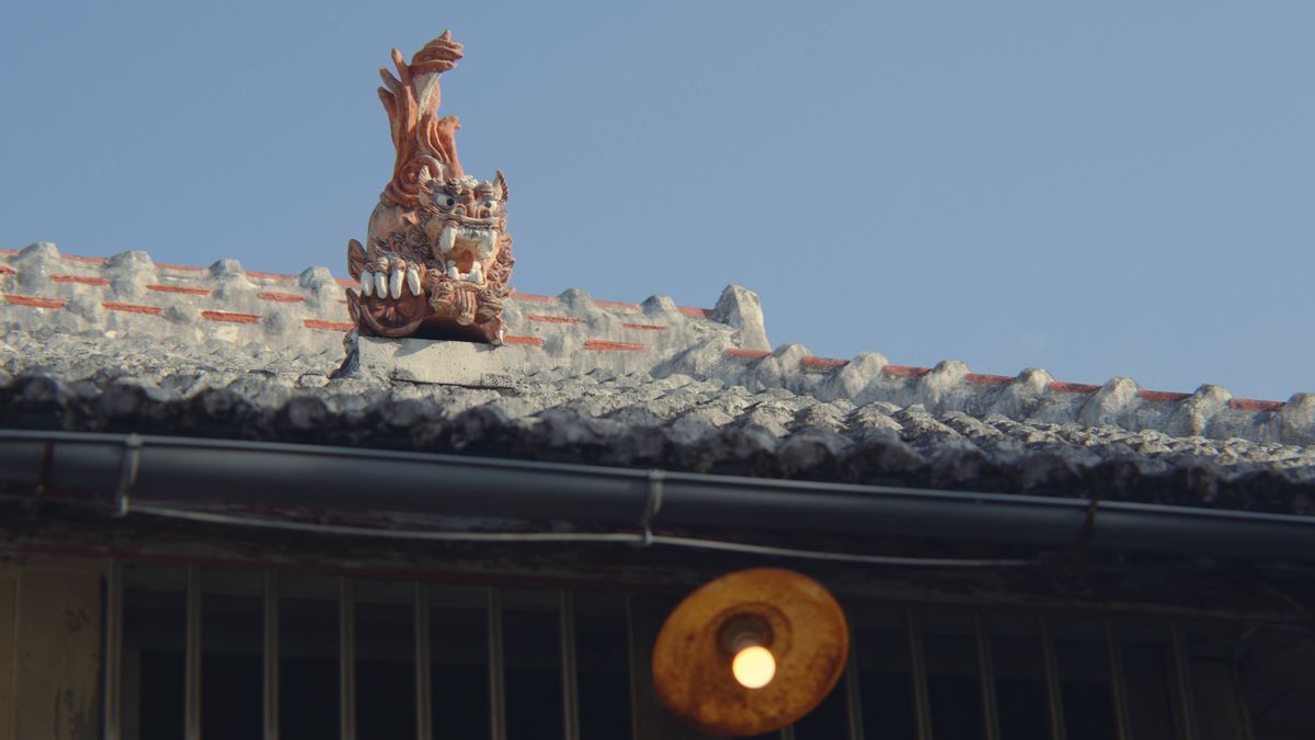 青空の下、赤瓦の屋根にのるシーサー