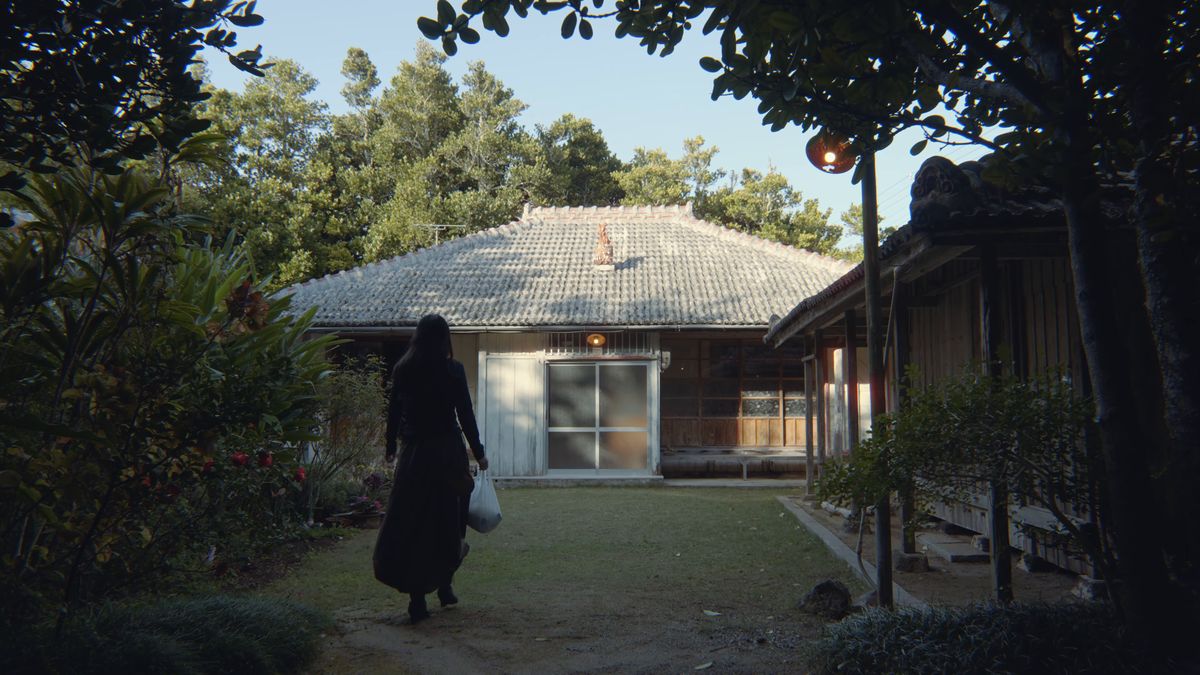 袋を提げて古民家の庭に戻る後ろ姿