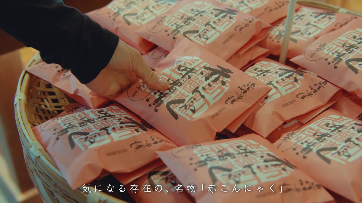 籠に積まれた桃色の袋の赤こんにゃくを手に取る