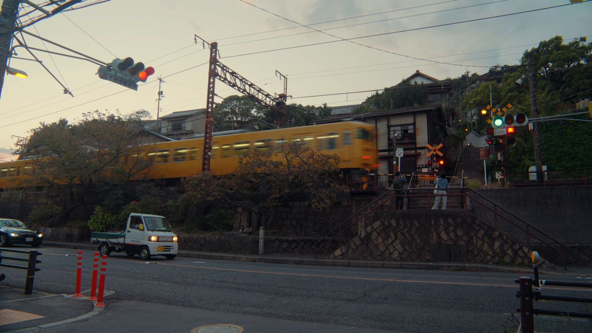 赤い信号の灯る踏切を通る黄色い電車