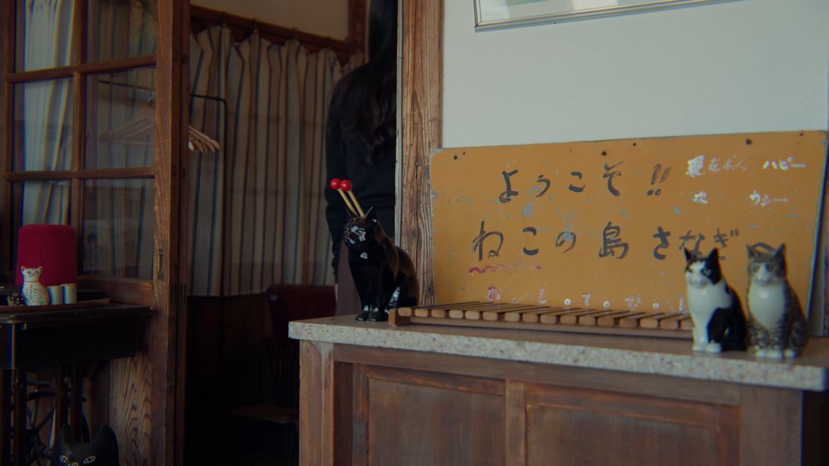 「ようこそ ねこの島さなぎ」の手書き看板と猫の置物