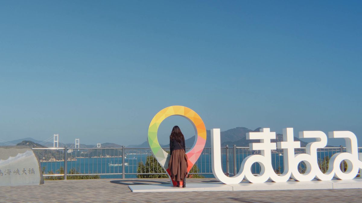 「しまなみ」の文字のオブジェの前に立つ後ろ姿と来島海峡大橋