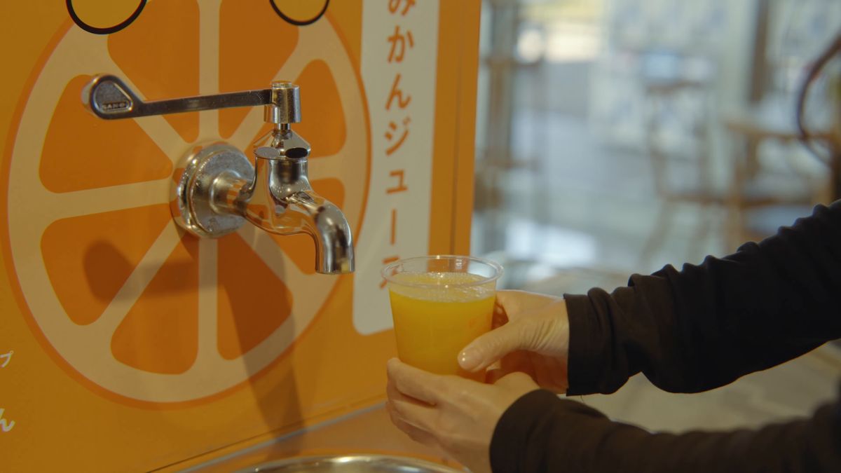 蛇口の下でコップにたまるみかんジュース