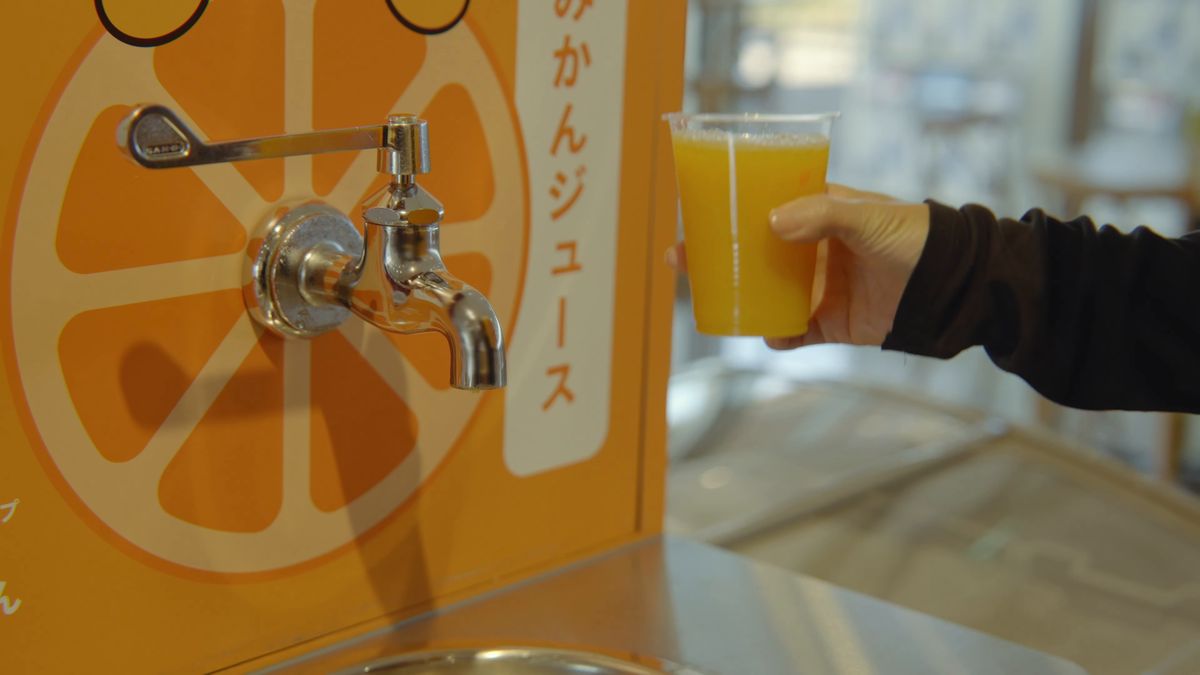 蛇口のそばでジュースのコップを持ち上げる手元