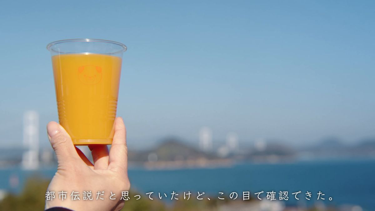 青空と海に向けて掲げたみかんジュース