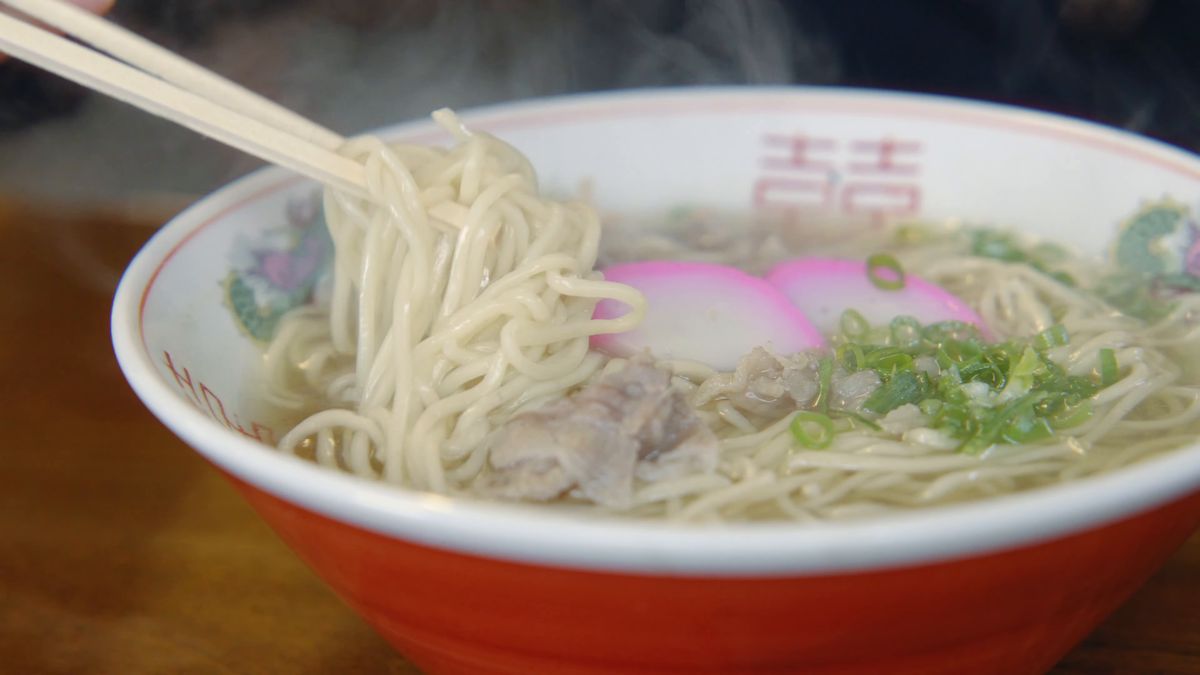 かまぼこと青ねぎの中華そばを箸で持ち上げる