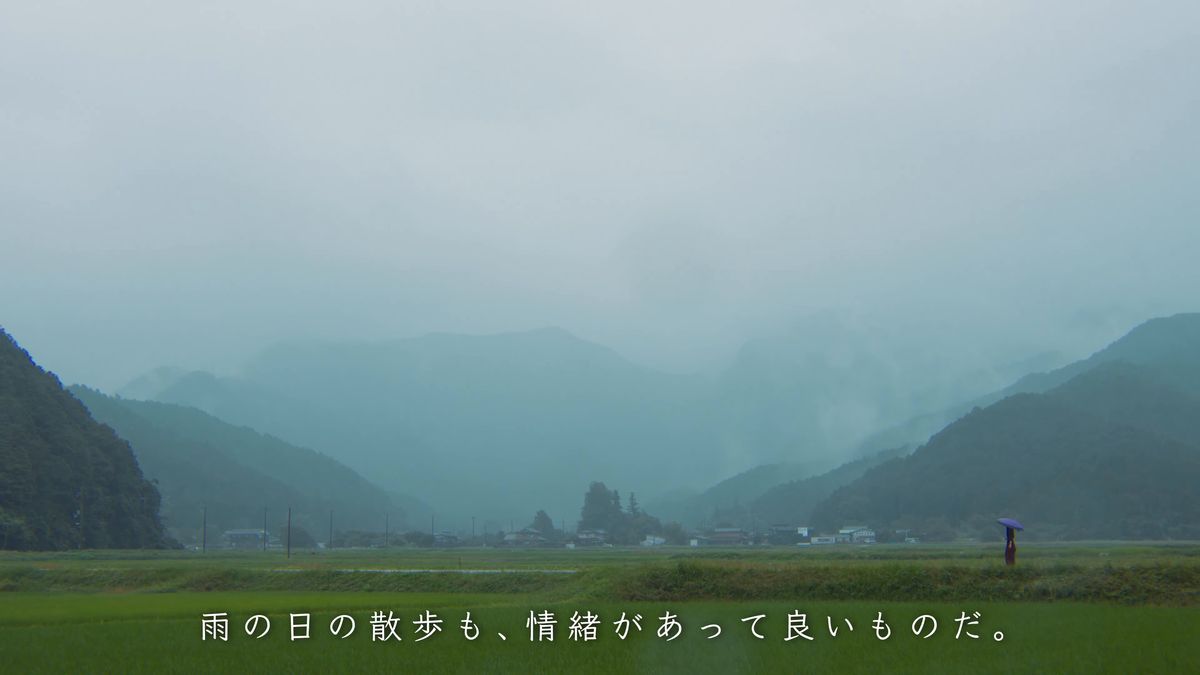 霧にかすむ山里と、傘をさして歩く人影