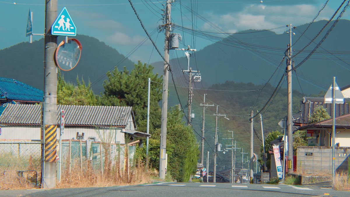 電柱と標識の並ぶ町の道と、遠くの山