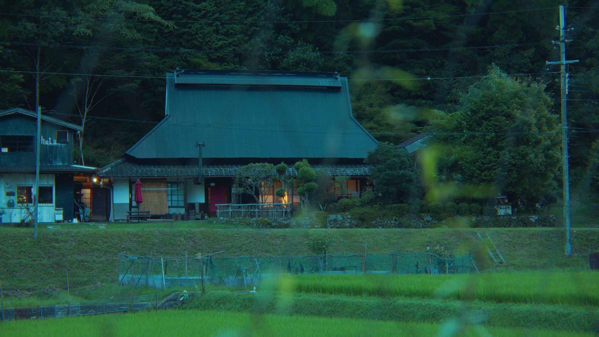 明かりのついた夕暮れの古民家と田んぼ
