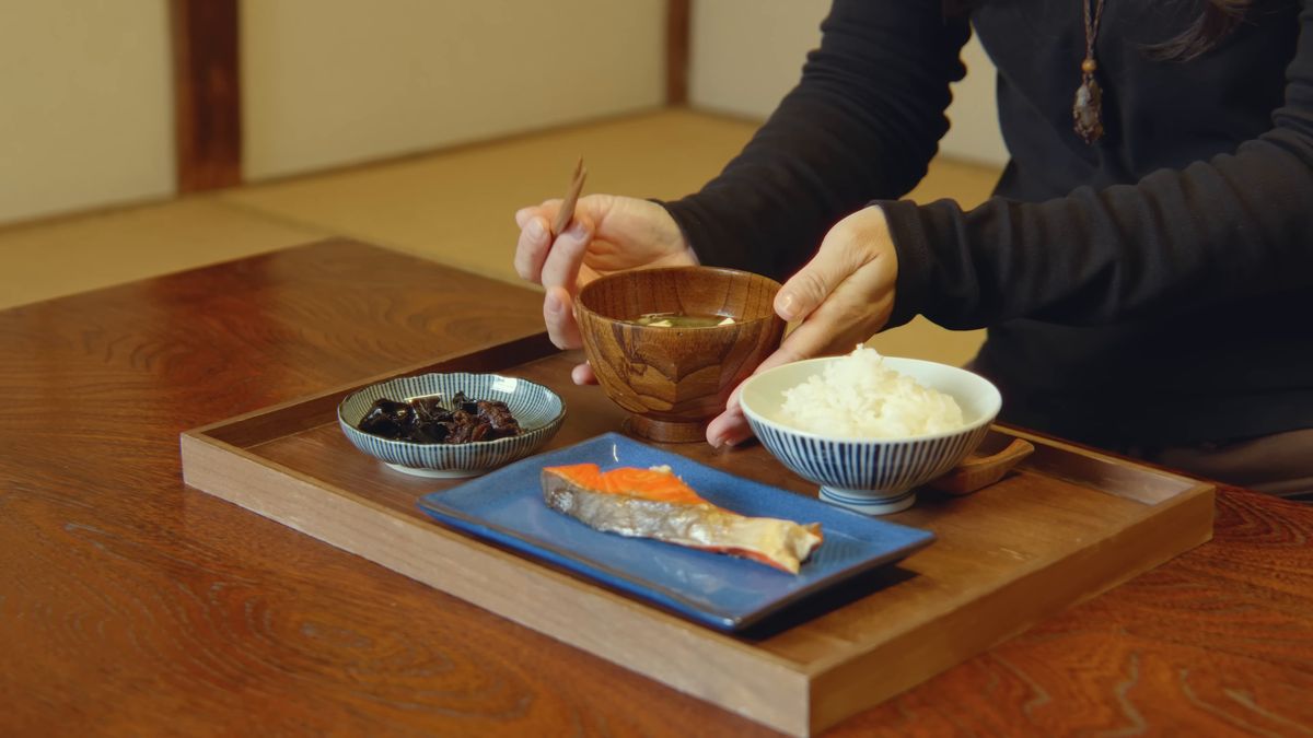 焼き鮭と佃煮とご飯の膳に、汁椀を置く手元