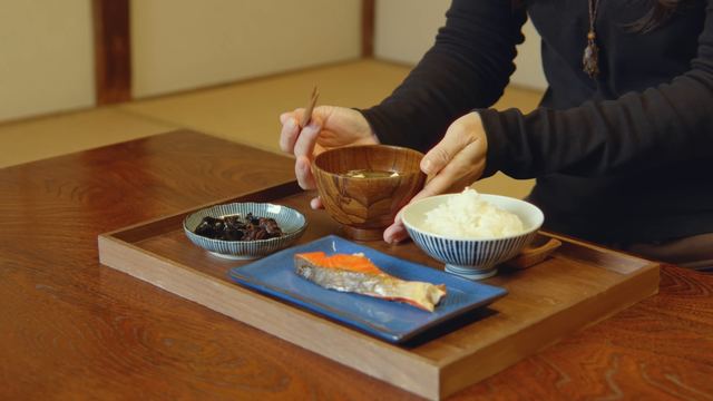 Setting a soup bowl on a tray of grilled salmon, tsukudani and rice