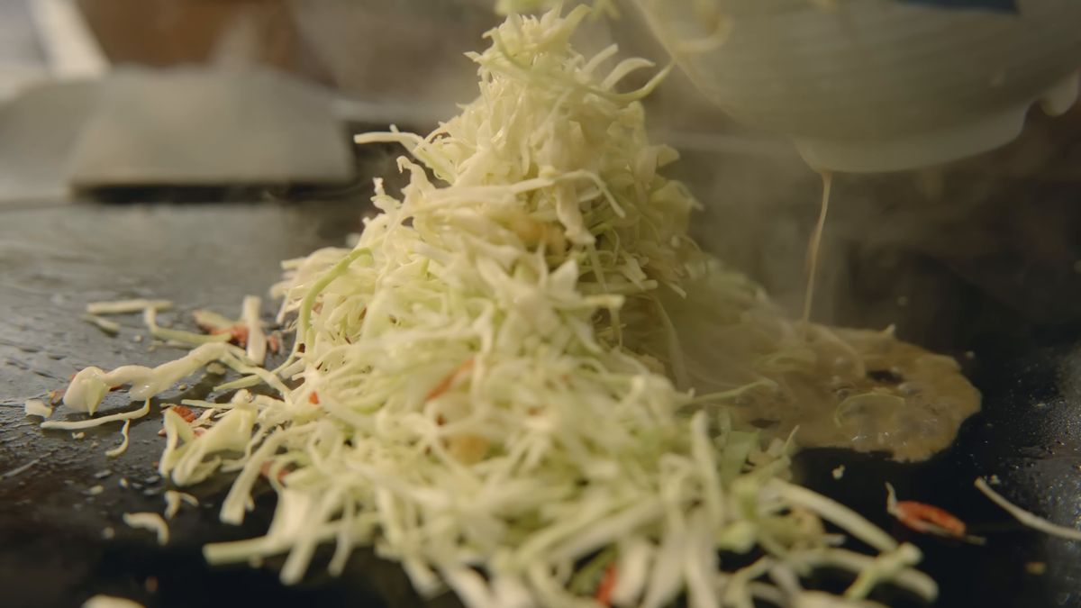 鉄板に山盛りの刻みキャベツと、注がれる生地